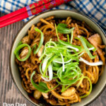 Portrait overhead image of dan dan noodles, a Chinese stir fried minced pork recipe served with a spring onion garnish with a text overlay