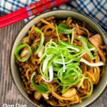 Portrait overhead image of dan dan noodles, a Chinese stir fried minced pork recipe served with a spring onion garnish with a text overlay