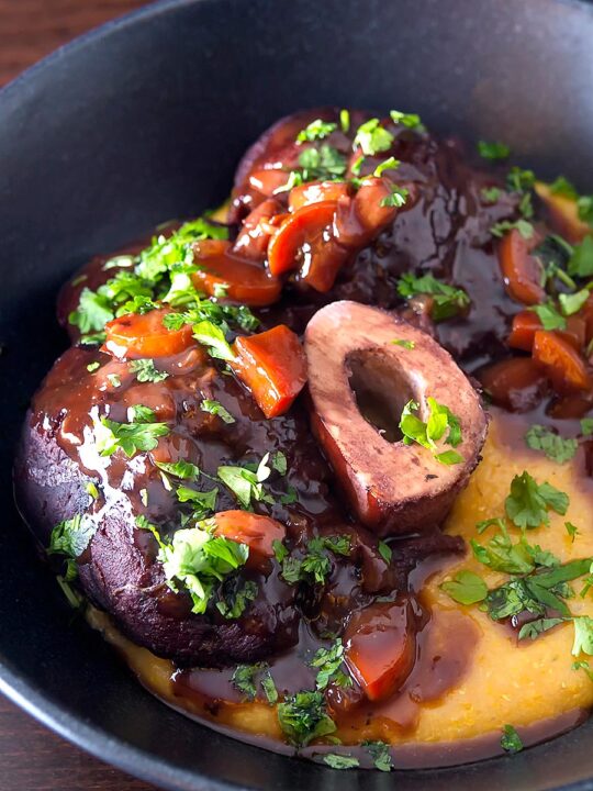 Portrait close up image of a beef shin osso bucco recipe served on polenta in a black bowl