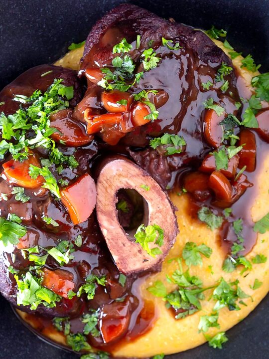 Portrait over head image of a beef shin osso bucco recipe served on polenta in a black bowl