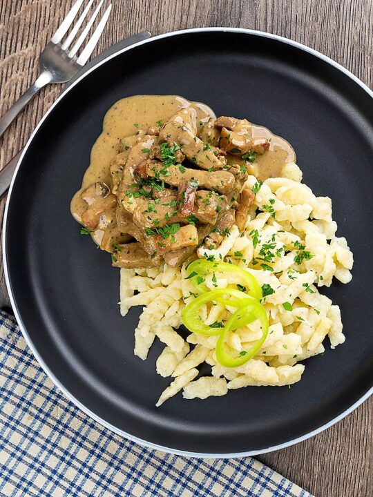 Portrait overhead image of a Hungarian Pork Stew called Borsos Tokany served on a black plate with nokedli noodles