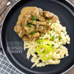 Portrait overhead image of a Hungarian Pork Stew called Borsos Tokany served on a black plate with nokedli noodles and a text overlay