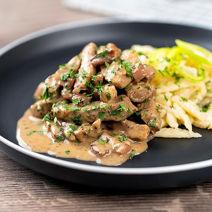 Square image of a Hungarian Pork Stew called Borsos Tokany served with nokedli dumplings on a black plate