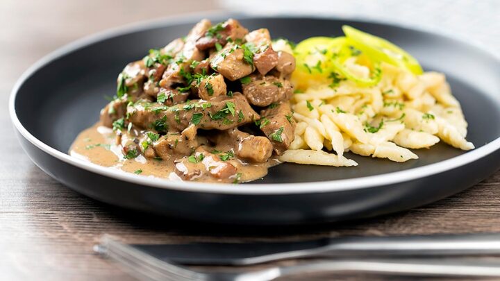 Landscape image of a Hungarian Pork Stew called Borsos Tokany served with nokedli dumplings on a black plate