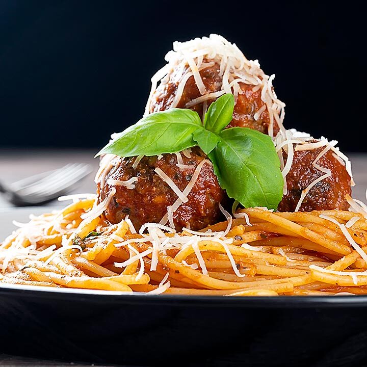 Square image of spaghetti and meatballs served with fresh basil and grated Parmesan cheese served on a white plate