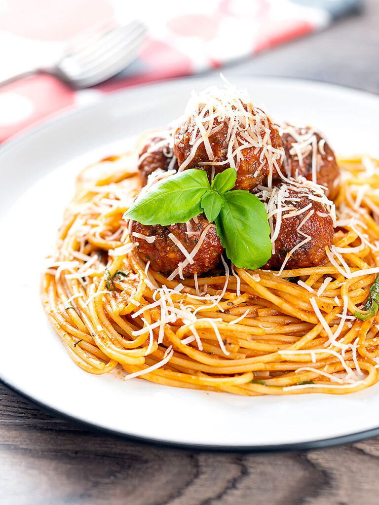 Portrait image of spaghetti and meatballs served with fresh basil and grated Parmesan cheese served on a white plate