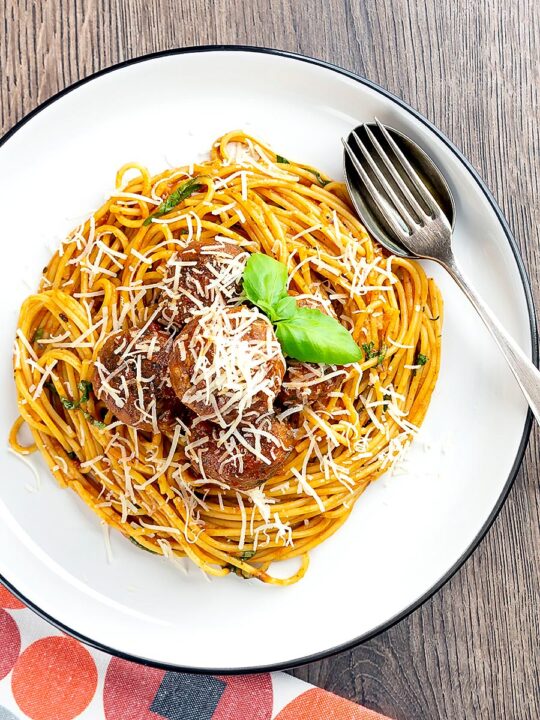 Portrait overhead image of spaghetti and meatballs served with fresh basil and grated Parmesan cheese served on a white plate