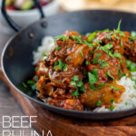 Portrait image of a beef bhuna curry served in an iron kadai with poppadoms and kachumber salad out of focus in the background featuring a title overlay