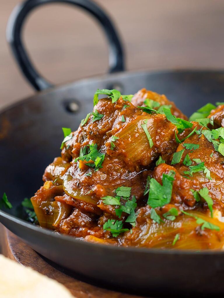 Portrait close up image of a beef bhuna curry served in an iron kadai garnished with chopped coriander