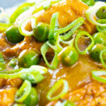 Portrait close up image of a takeaway influenced Chinese chicken curry with garden peas and spring onions featuring a text overlay