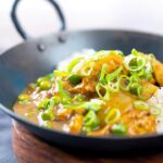 Square image of a takeaway influenced Chinese chicken curry with garden peas and spring onions