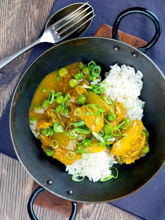 Portrait overhead image of a takeaway influenced Chinese chicken curry with garden peas and spring onions