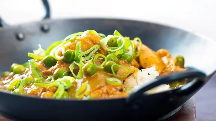 Landscape image of a takeaway influenced Chinese chicken curry with garden peas and spring onions