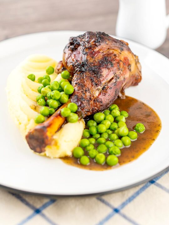 Portrait image of minted lamb shanks served with mashed potatoes and peas