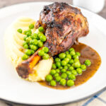 Portrait image of minted lamb shanks served with mashed potatoes and peas featuring a text overlay