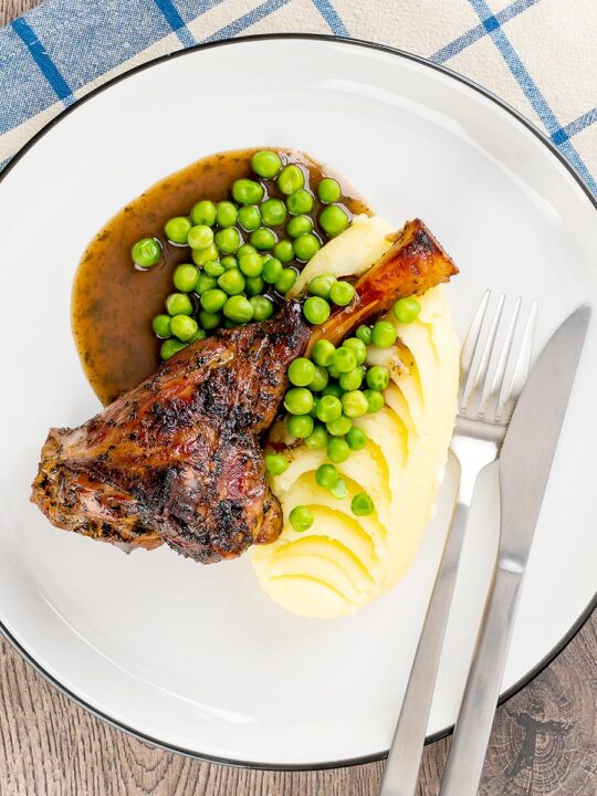 Portrait overhead image of minted lamb shanks served with mashed potatoes and peas