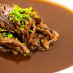 Portrait close up image of a British oxtail soup with a pile of shredded oxtail and snipped chives