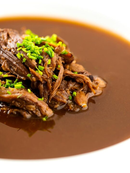 Portrait close up image of a British oxtail soup with a pile of shredded oxtail and snipped chives