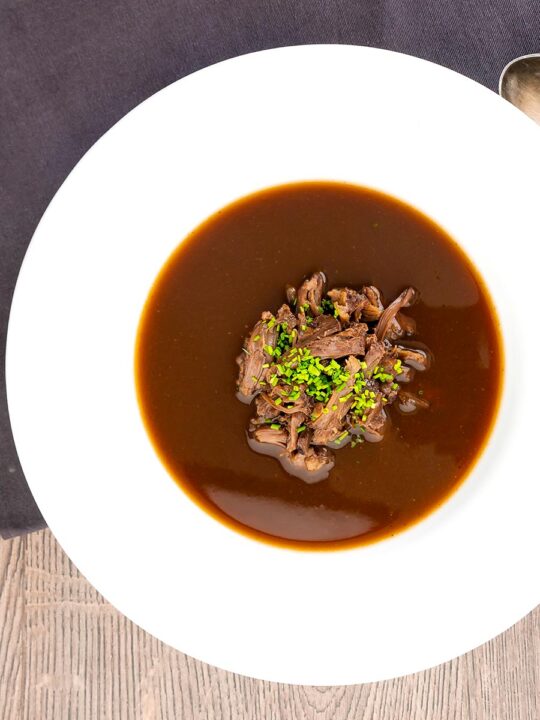 Portrait overhead image of a British oxtail soup with a pile of shredded oxtail and snipped chives