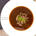 Portrait overhead image of a British oxtail soup with a pile of shredded oxtail and snipped chives featuring a title overlay