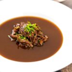 Portrait image of a British oxtail soup with a pile of shredded oxtail and snipped chives