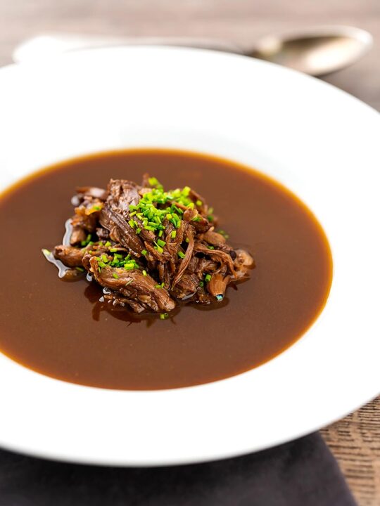 Portrait image of a British oxtail soup with a pile of shredded oxtail and snipped chives