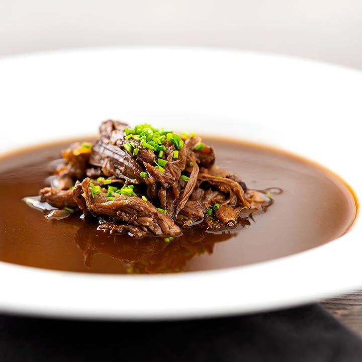 Square image of a British oxtail soup with a pile of shredded oxtail and snipped chives