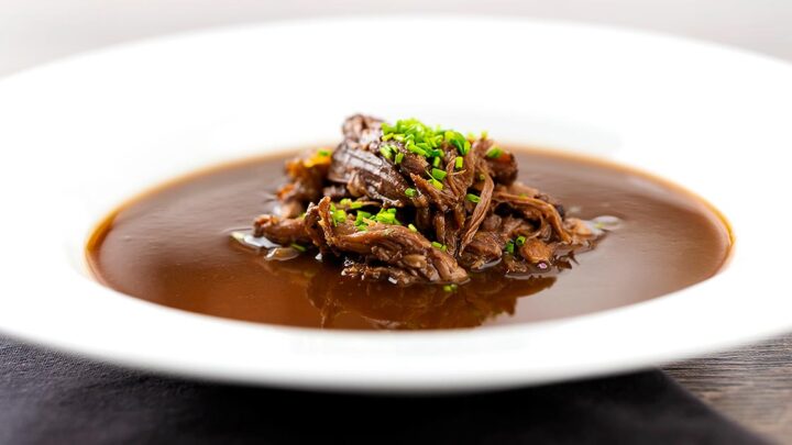 Landscape image of a British oxtail soup with a pile of shredded oxtail and snipped chives