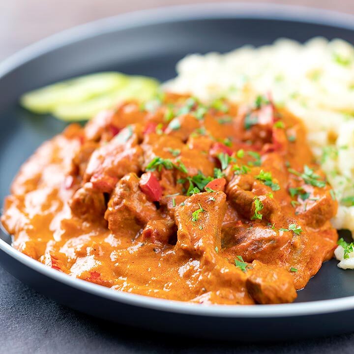 Square image of a Hungarian inspired pork paprikash or sertéspaprikás served with nokedli on a grey plate
