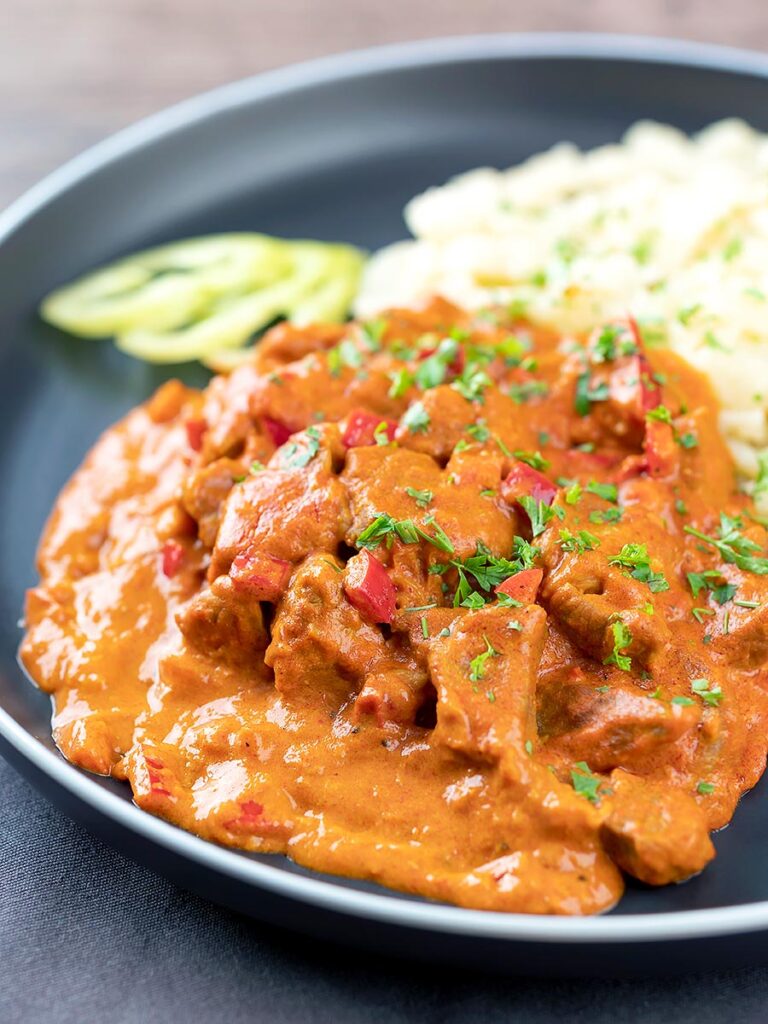 Portrait image of a Hungarian inspired pork paprikash or sertéspaprikás served with nokedli on a grey plate