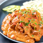 Portrait image of a Hungarian inspired pork paprikash or sertéspaprikás served with nokedli on a grey plate featuring a title overlay