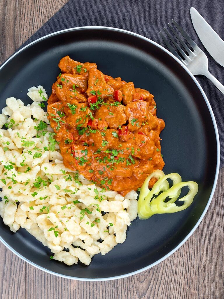 Portrait overhead image of a Hungarian inspired pork paprikash or sertéspaprikás served with nokedli on a grey plate