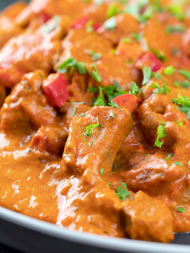 Portrait close up image of a Hungarian inspired pork paprikash or sertéspaprikás served with nokedli on a grey plate