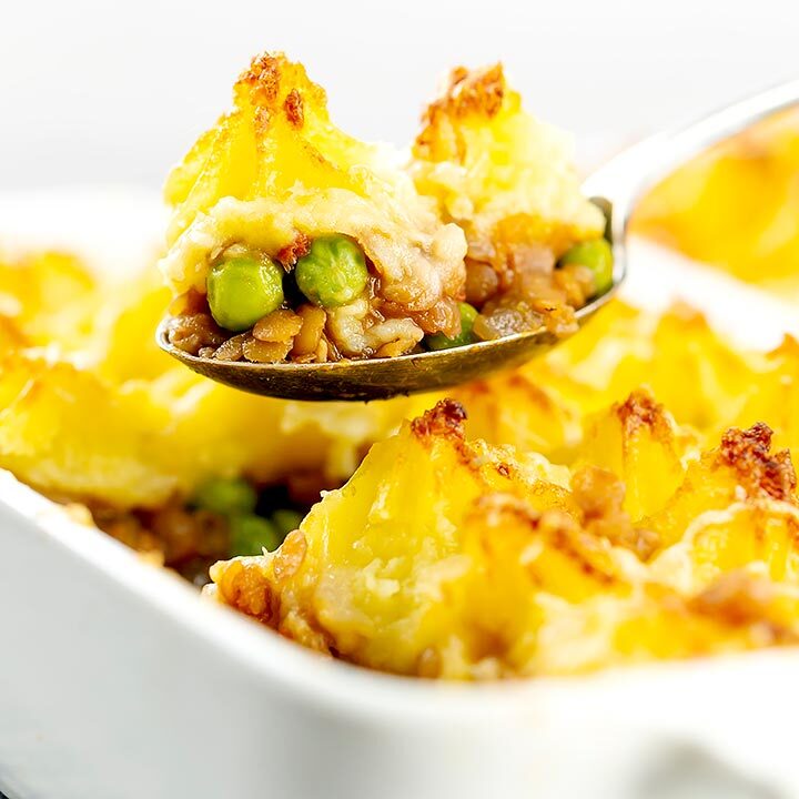 Close up square image of a spoon full of vegetarian shepherds pie or shepherdess pie being taken from a whole pie