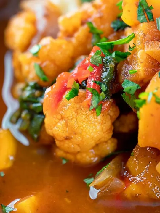 Portrait close up image of a spicy vegetable soup with sweet potato, cauliflower and spinach in a harissa broth