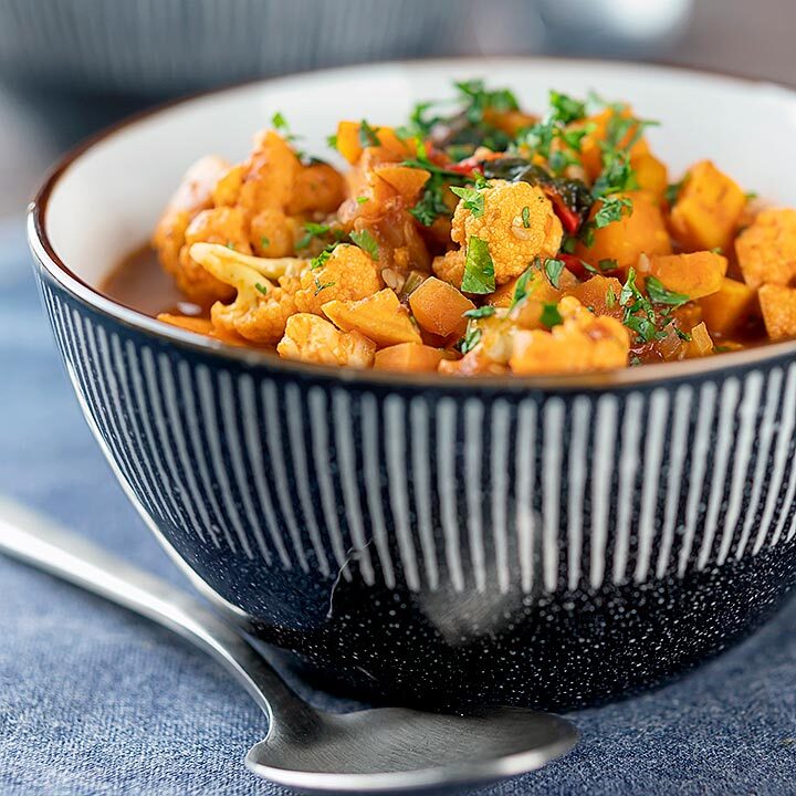 Square image of a spicy vegetable soup with sweet potato, cauliflower and in a harissa broth