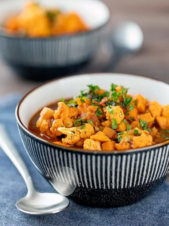 Portrait image of a spicy vegetable soup with sweet potato, cauliflower and in a harissa broth