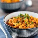 Portrait image of a spicy vegetable soup with sweet potato, cauliflower and in a harissa broth featuring a title overlay