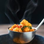 Portrait image of a steaming hot spicy vegetable soup with sweet potato, cauliflower and in a harissa broth in a ladle