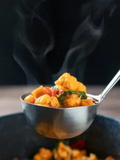 Portrait image of a steaming hot spicy vegetable soup with sweet potato, cauliflower and in a harissa broth in a ladle