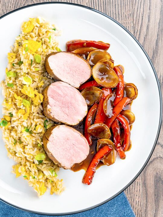 Portrait overhead of image rosy pink roasted juicy sweet and sour pork tenderloin with onions and red pepper in a rich sweet and sour sauce and egg fried rice