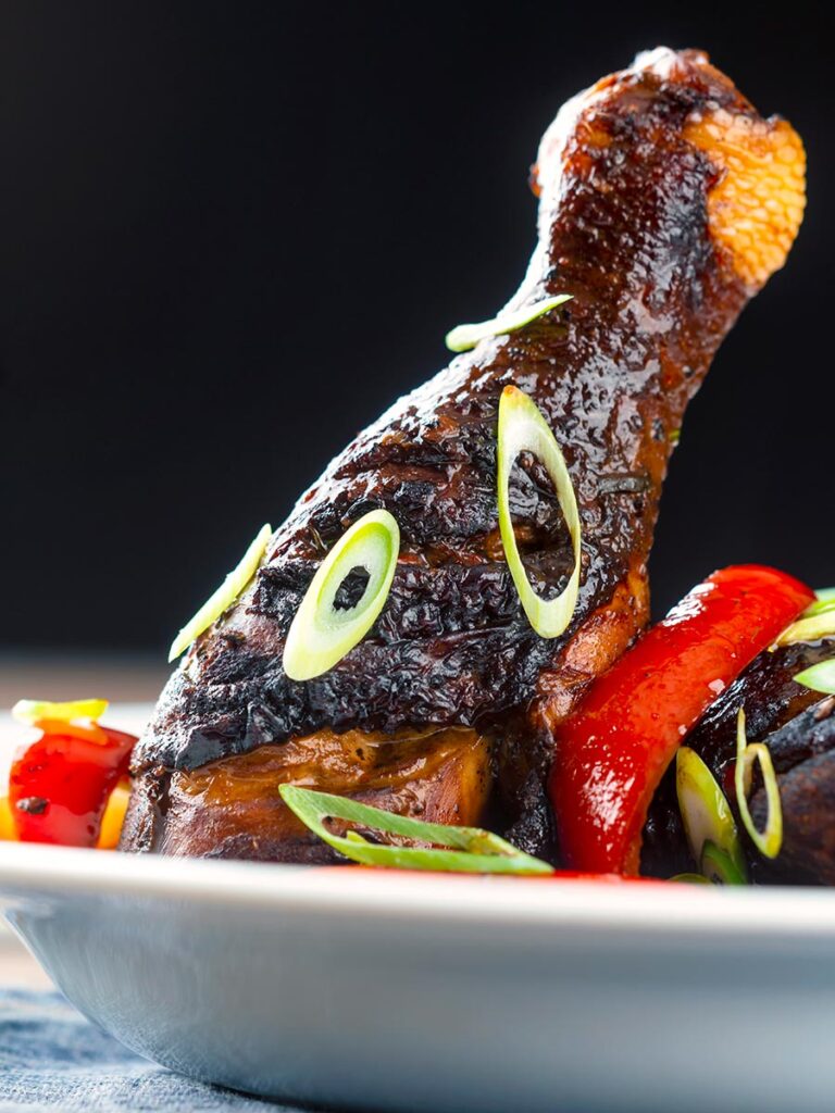 Portrait close up image of a Jamaican brown stew chicken served in a white shallow bowl with a spring onion garnish
