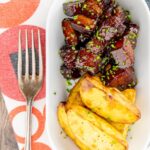 Portrait overhead image of sticky gluhwein pork belly bites served with potato wedges and snipped chives