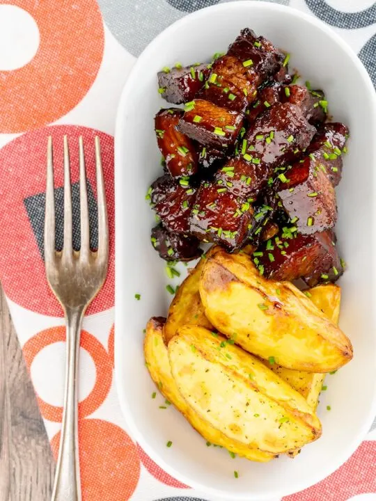 Portrait overhead image of sticky gluhwein pork belly bites served with potato wedges and snipped chives