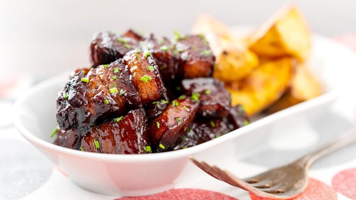 Landscape image of sticky gluhwein pork belly bites served with potato wedges and snipped chives