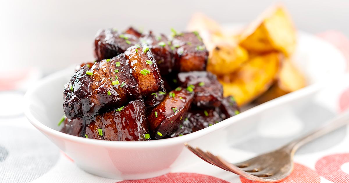 Landscape image of sticky gluhwein pork belly bites served with potato wedges and snipped chives