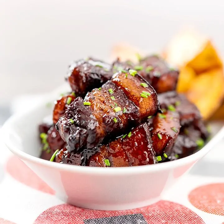 Square image of sticky gluhwein pork belly bites served with potato wedges and snipped chives