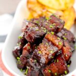 Portrait image of sticky gluhwein pork belly bites served with potato wedges and snipped chives