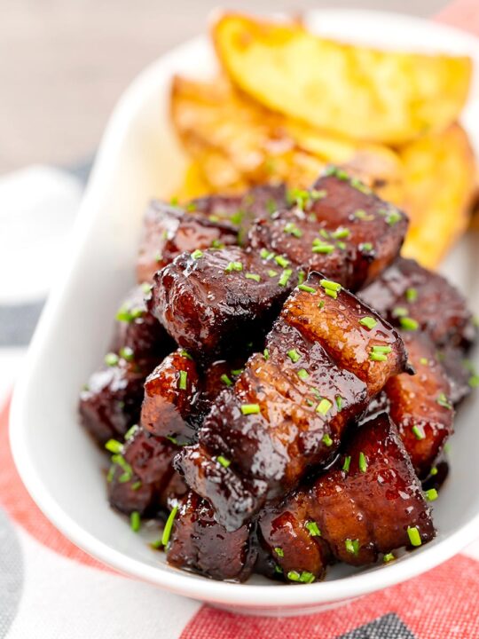 Portrait image of sticky gluhwein pork belly bites served with potato wedges and snipped chives