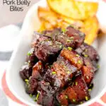 Portrait image of sticky gluhwein pork belly bites served with potato wedges and snipped chives featuring a text overlay
